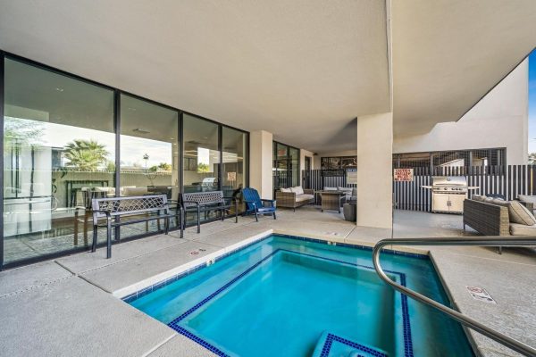 Poolside patio with a blue rectangular pool, glass-walled building, and outdoor seating on a covered deck.